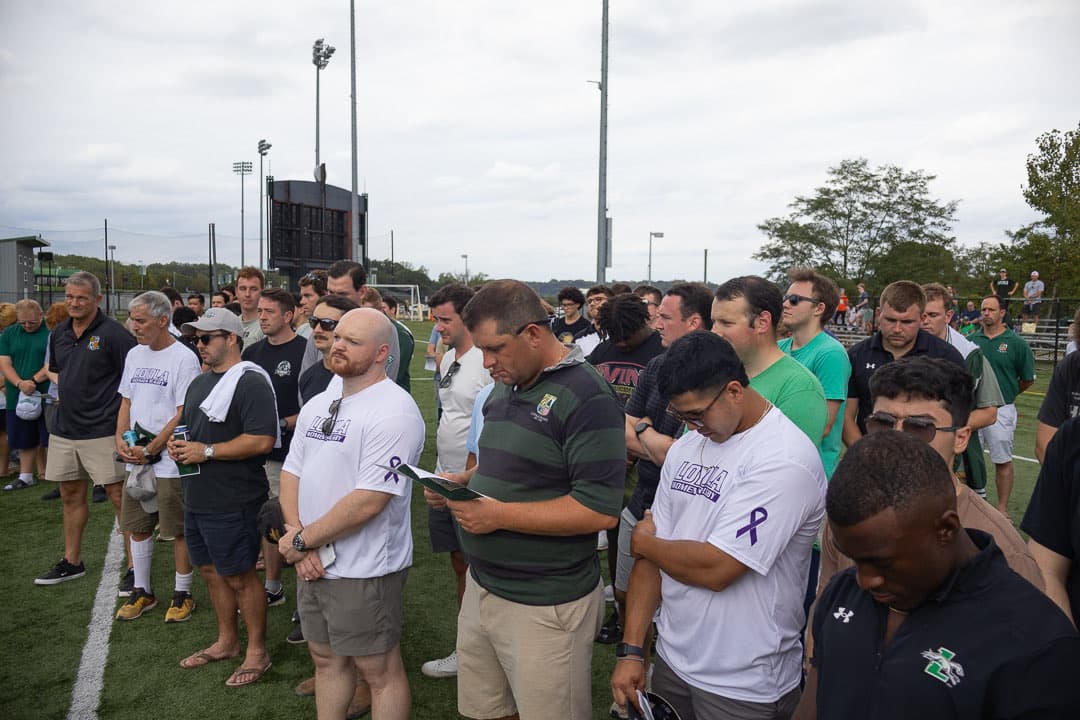 Alumni with heads bowed along the touchline